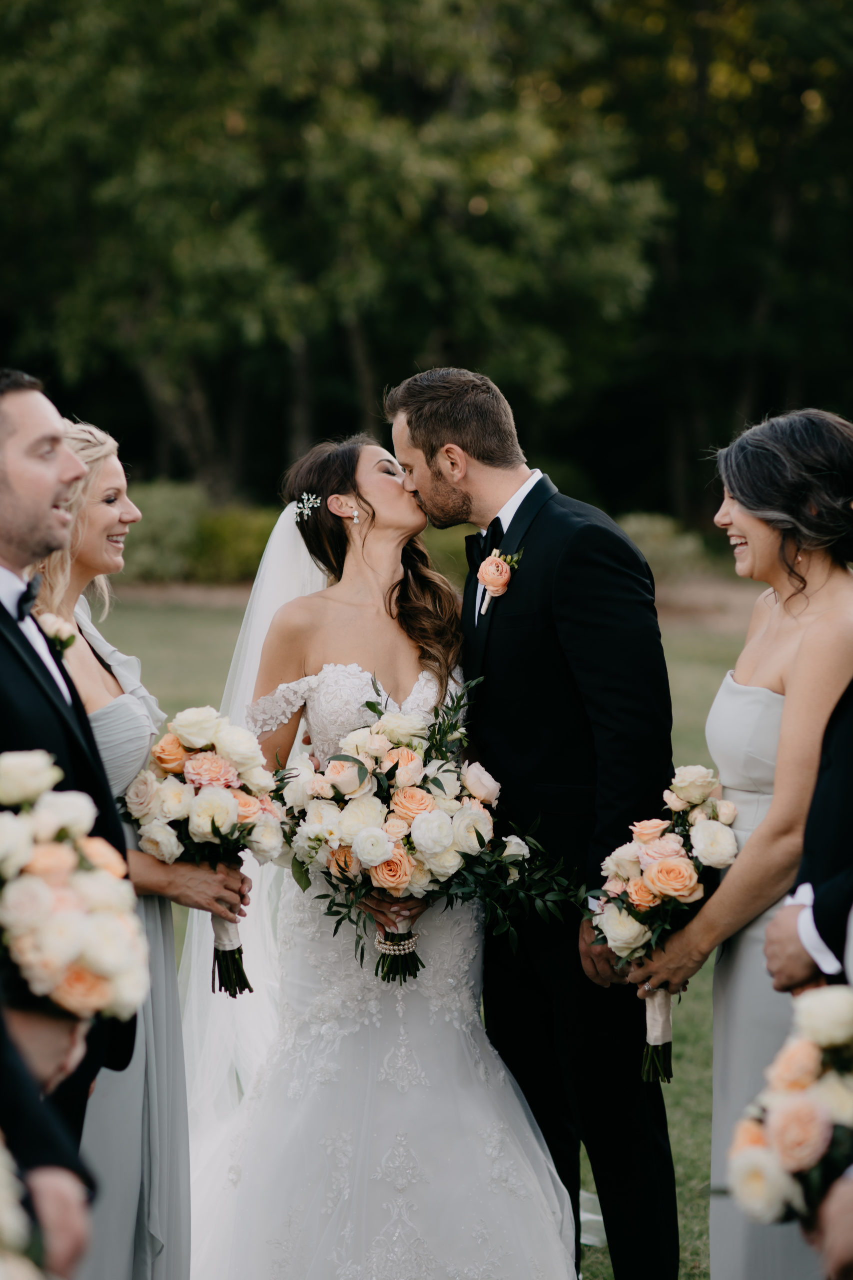 A bride and groom kissing in front of their wedding party.