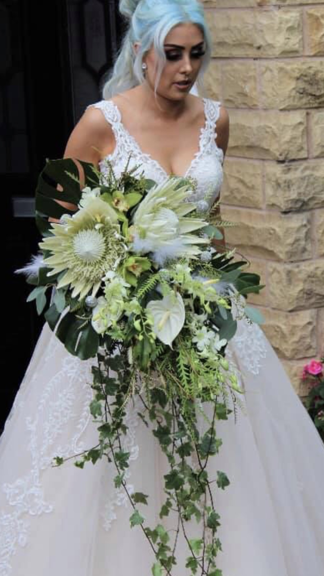 A bride holding her bouquet of flowers in front of a stone wall.