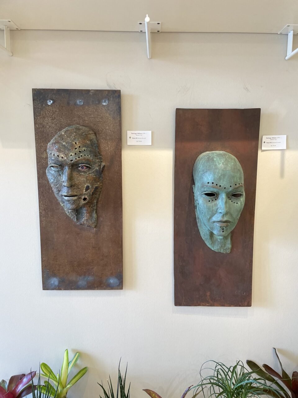Two sculptures of faces hanging on a wall.