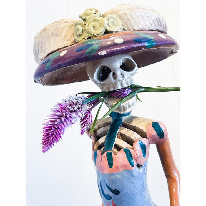 A skeleton wearing a hat and holding flowers.